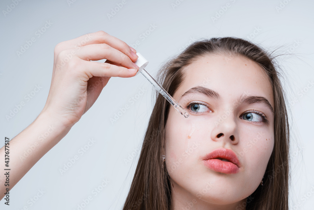 Beautiful young girl cleanses the skin getting rid of acne while holding a dropper with serum in her hand
