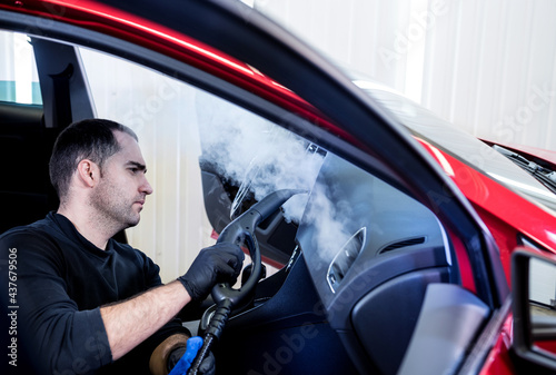 Car service worker cleans interiror with steam cleaner