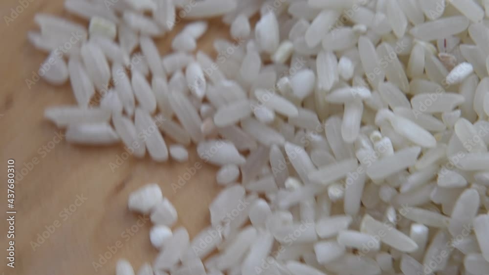 Raw rice grains rotate on a wooden surface. Video is blurry in soft focus at high magnification. Raw rice grains rotate on a wooden surface. Video is blurry in soft focus at high magnification.