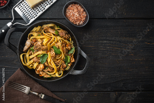 Tagliatelle with chanterelles and stewed rabbit, in frying cast iron pan or pot, on black wooden table , top view flat lay, with copy space for text