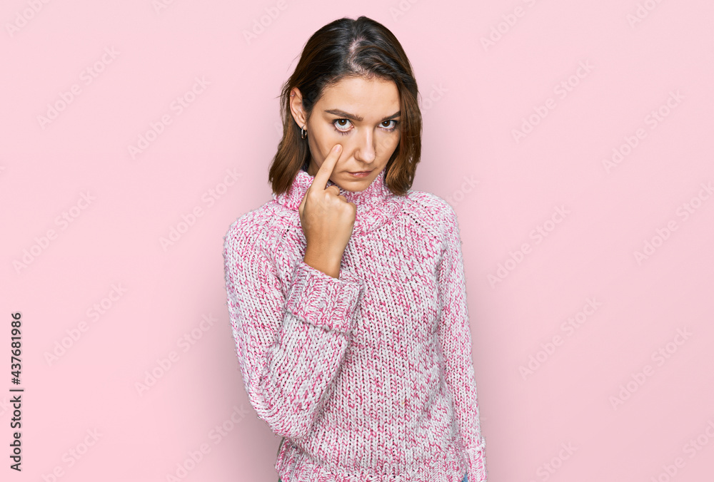 Young caucasian girl wearing wool winter sweater pointing to the eye watching you gesture, suspicious expression Young caucasian girl wearing wool winter sweater pointing to the eye watching you gesture, suspicious expression