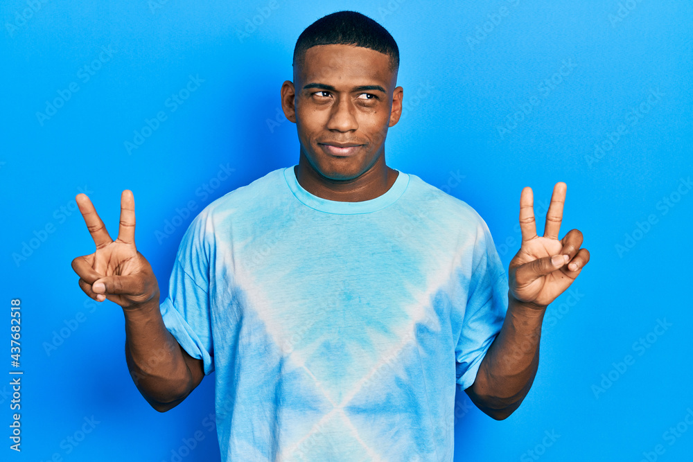 Young black man doing victory sign and peace gesture smiling looking to the side and staring away thinking. Young black man doing victory sign and peace gesture smiling looking to the side and staring away thinking.