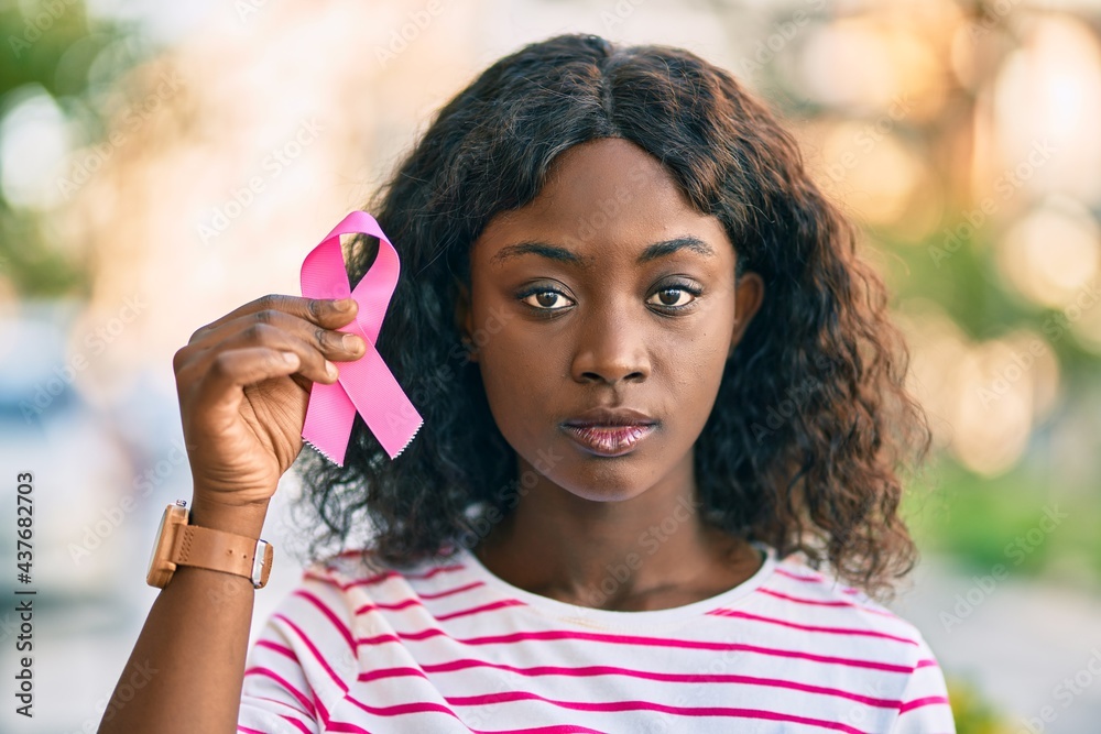 Young african american girl with serious expression holding pink breast cancer ribbon at the city. Young african american girl with serious expression holding pink breast cancer ribbon at the city.