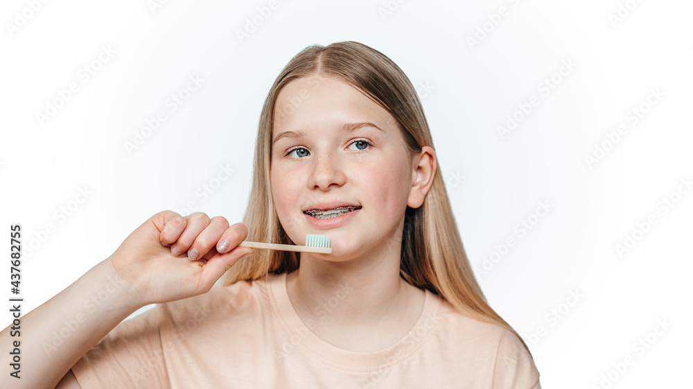 Smiling blonde girl with orthodontic braces holding holding an eco friendly bamboo toothbrush Smiling blonde girl with orthodontic braces holding holding an eco friendly bamboo toothbrush