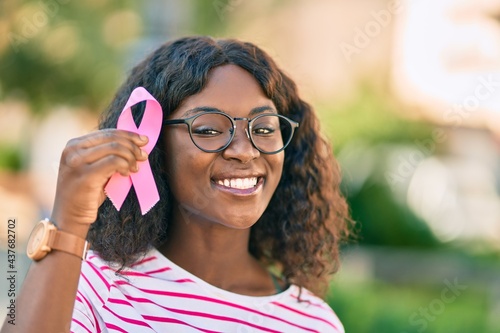 Young african american girl smiling happy holding pink breast cancer ribbon at the city.
