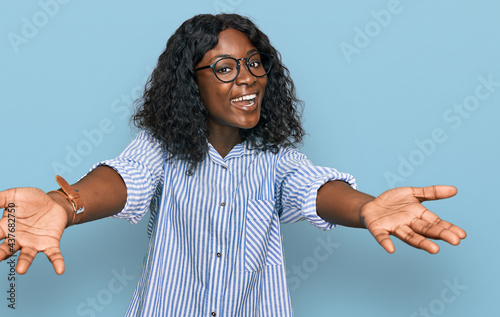 Beautiful african young woman wearing casual clothes and glasses smiling cheerful offering hands giving assistance and acceptance.