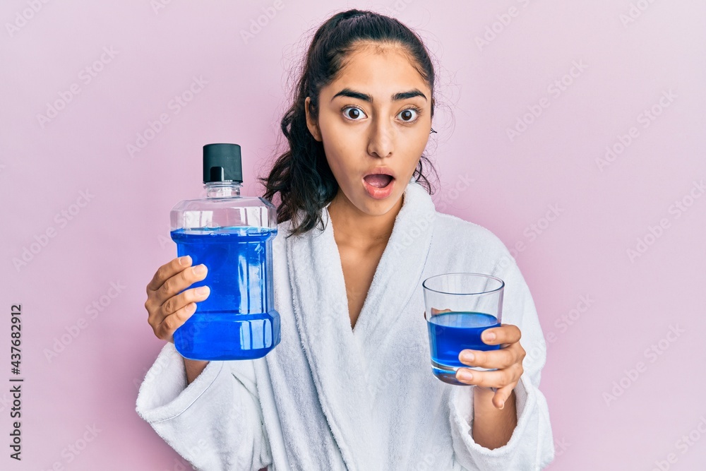 Hispanic teenager girl with dental braces holding mouthwash afraid and shocked with surprise and amazed expression, fear and excited face. Hispanic teenager girl with dental braces holding mouthwash afraid and shocked with surprise and amazed expression, fear and excited face.