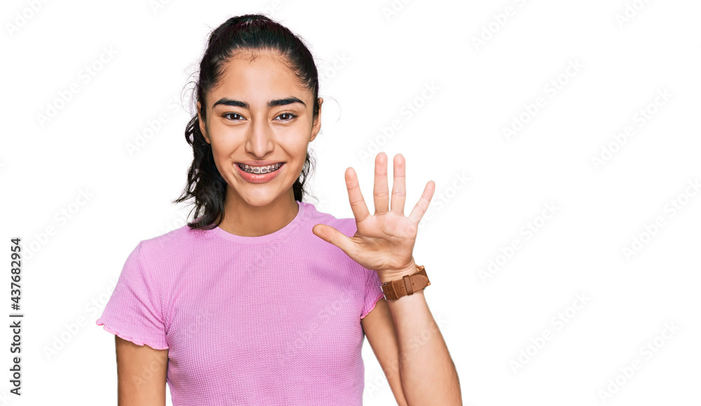 Hispanic teenager girl with dental braces wearing casual clothes showing and pointing up with fingers number five while smiling confident and happy. Hispanic teenager girl with dental braces wearing casual clothes showing and pointing up with fingers number five while smiling confident and happy.