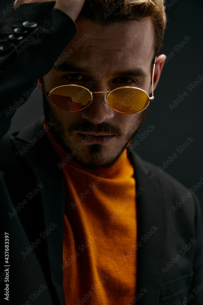 Fototapeta premium a brutal guy with glasses and a black jacket orange sweater dark background 