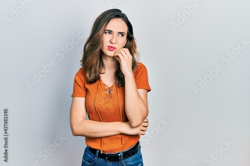 Young hispanic girl wearing casual clothes serious face thinking about question with hand on chin, thoughtful about confusing idea