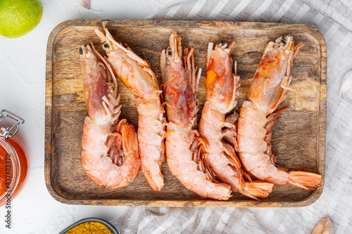 Argentinian raw red prawns, shrimps with heads, on wooden tray, on white background, top view flat lay