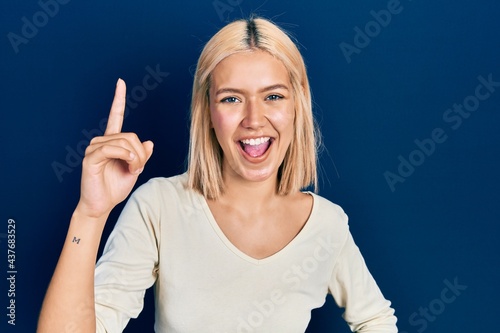 Beautiful blonde woman wearing casual sweater pointing finger up with successful idea. exited and happy. number one.