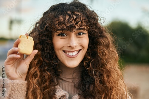 Young hispanic woman smiling happy holding earphones at the city.