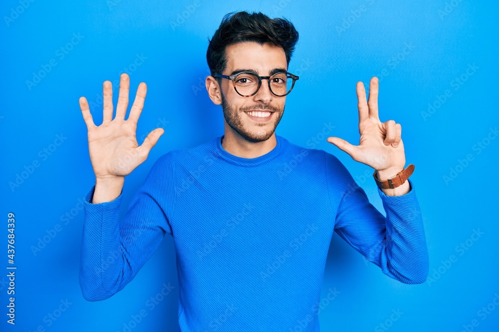 Naklejka premium Young hispanic man wearing casual clothes and glasses showing and pointing up with fingers number eight while smiling confident and happy.