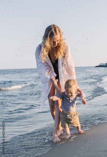 young mother teaches baby to walk on the beach