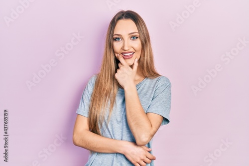 Young blonde girl wearing casual t shirt looking confident at the camera smiling with crossed arms and hand raised on chin. thinking positive.