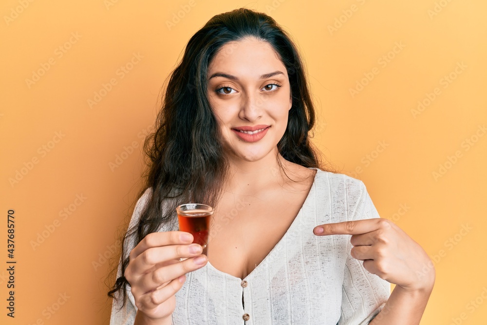Beautiful middle eastern woman drinking whiskey shot pointing finger to one self smiling happy and proud Beautiful middle eastern woman drinking whiskey shot pointing finger to one self smiling happy and proud