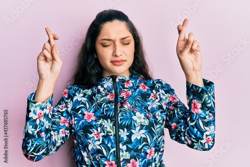 Beautiful middle eastern woman wearing casual floral jacket gesturing finger crossed smiling with hope and eyes closed. luck and superstitious concept.