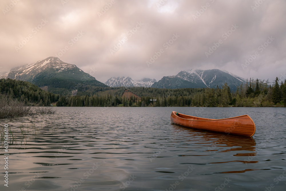 Mountain lake with a boat and snowy mountains in the background and cloudy skies. 