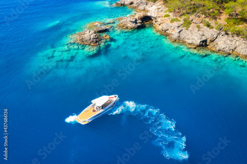 Speed boat on blue sea at sunrise in summer. Aerial view of motorboat on sea bay, rocks in clear azure water. Tropical landscape with yacht, stones, mountain, green trees. Top view. Oludeniz, Turkey © den-belitsky