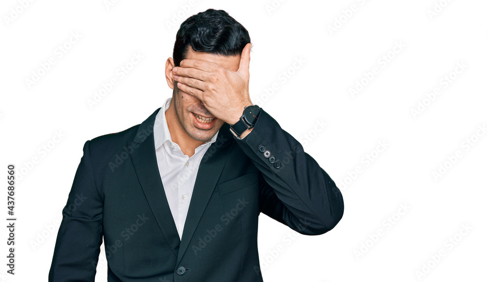 Handsome hispanic man wearing business clothes smiling and laughing with hand on face covering eyes for surprise. blind concept. Handsome hispanic man wearing business clothes smiling and laughing with hand on face covering eyes for surprise. blind concept.