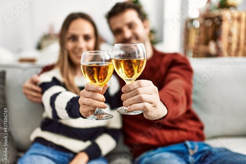 Young hispanic couple smiling happy toasting with champagne sitting on the sofa at home.