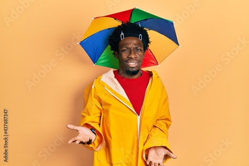 Young african american man wearing yellow raincoat clueless and confused with open arms, no idea concept.