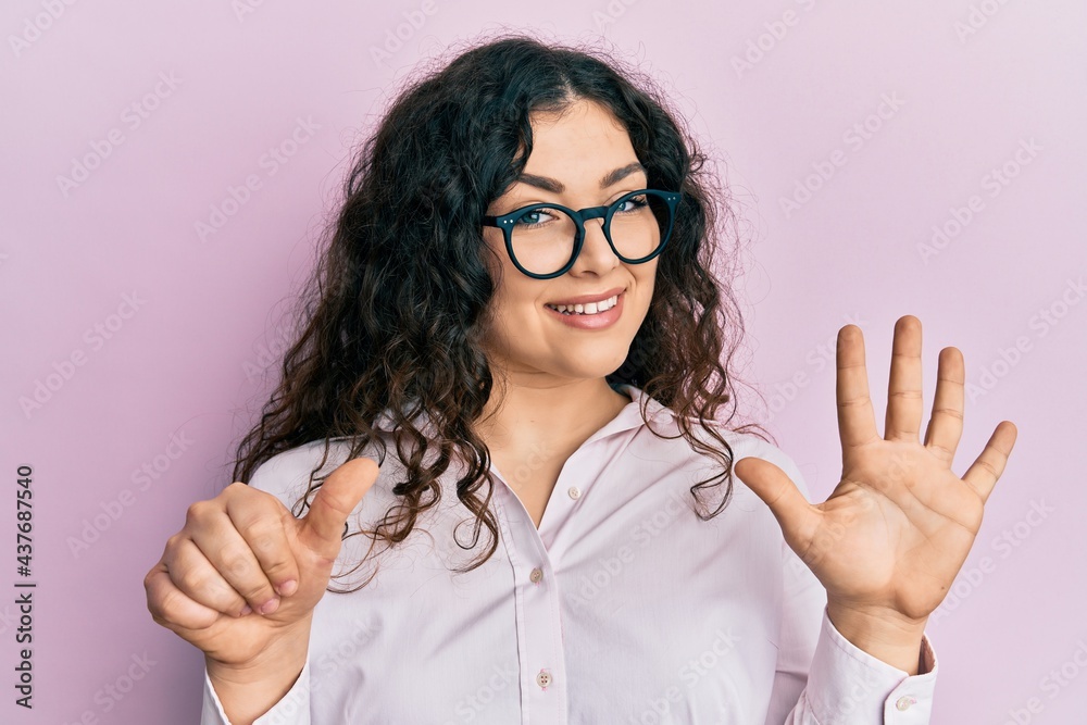 Young brunette woman with curly hair wearing casual clothes and glasses showing and pointing up with fingers number six while smiling confident and happy. Young brunette woman with curly hair wearing casual clothes and glasses showing and pointing up with fingers number six while smiling confident and happy.