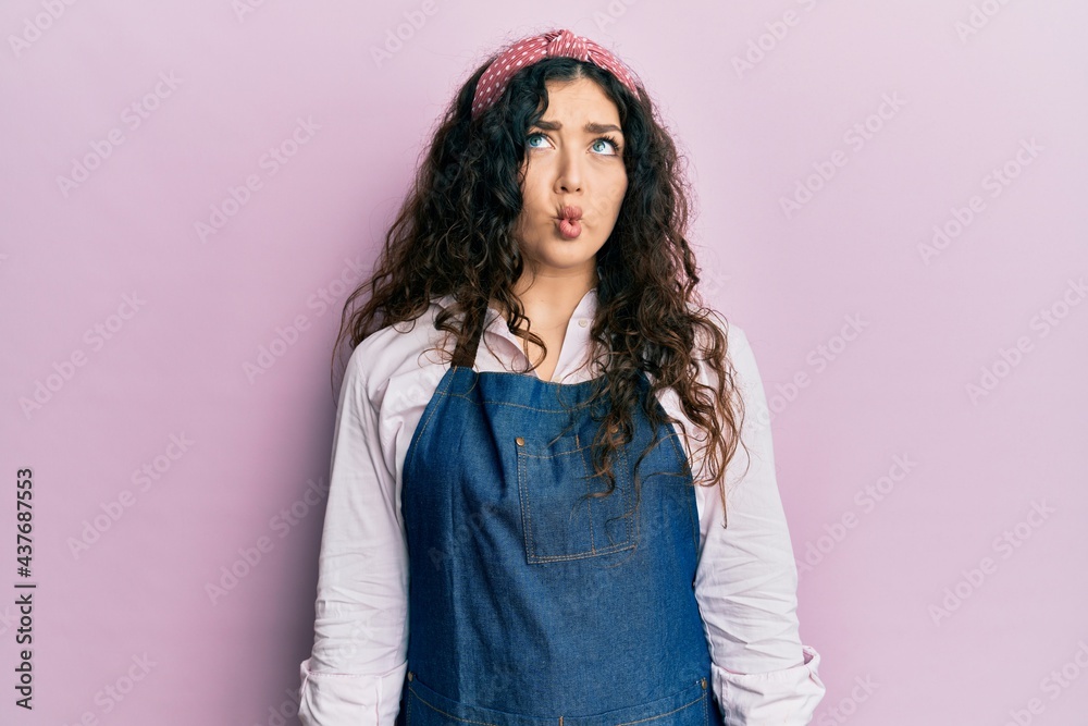 Young brunette woman with curly hair wearing cleaner apron and gloves making fish face with lips, crazy and comical gesture. funny expression. Young brunette woman with curly hair wearing cleaner apron and gloves making fish face with lips, crazy and comical gesture. funny expression.