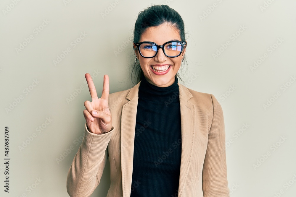 Young hispanic woman wearing business style and glasses smiling with happy face winking at the camera doing victory sign. number two. Young hispanic woman wearing business style and glasses smiling with happy face winking at the camera doing victory sign. number two.