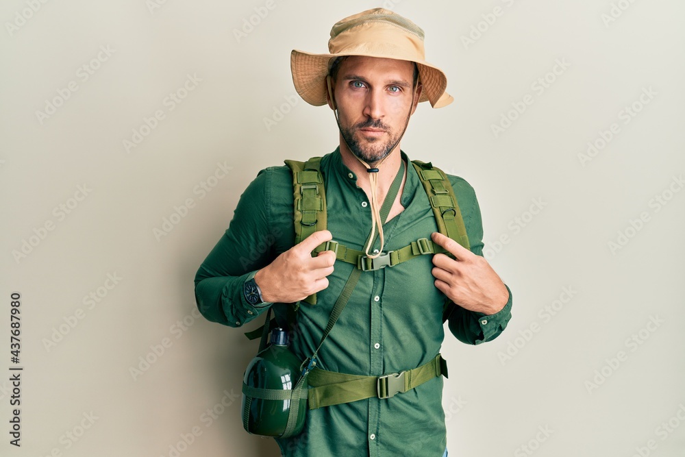 Fototapeta premium Handsome man with beard wearing explorer hat and backpack relaxed with serious expression on face. simple and natural looking at the camera.