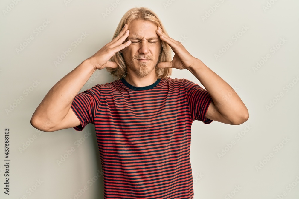 Caucasian young man with long hair wearing casual striped t shirt with hand on head, headache because stress. suffering migraine. Caucasian young man with long hair wearing casual striped t shirt with hand on head, headache because stress. suffering migraine.