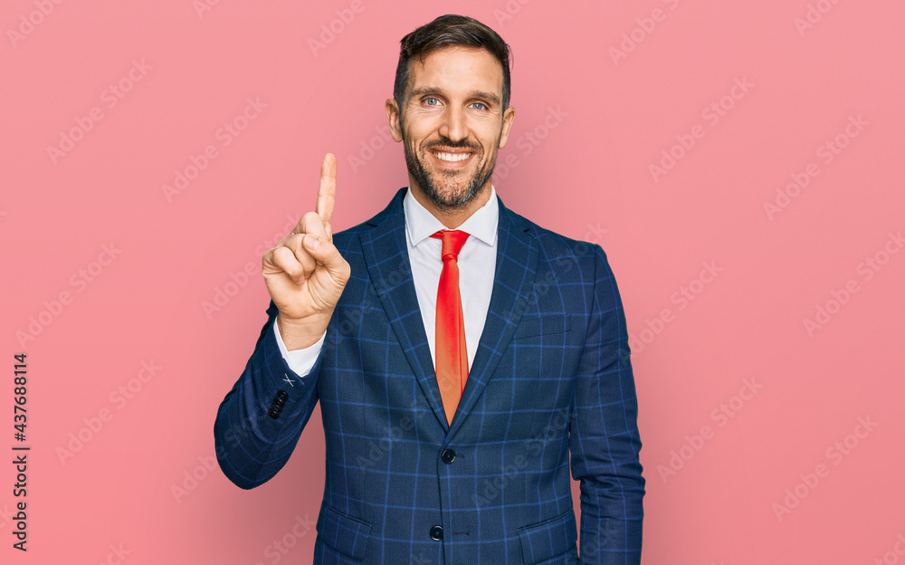 Handsome man with beard wearing business suit and tie showing and pointing up with finger number one while smiling confident and happy. Handsome man with beard wearing business suit and tie showing and pointing up with finger number one while smiling confident and happy.