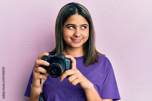 Young latin woman using reflex camera smiling looking to the side and staring away thinking.
