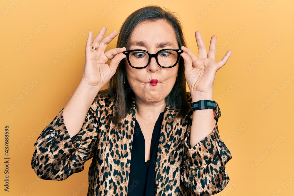 Middle age hispanic woman wearing business clothes and holding glasses making fish face with mouth and squinting eyes, crazy and comical. Middle age hispanic woman wearing business clothes and holding glasses making fish face with mouth and squinting eyes, crazy and comical.