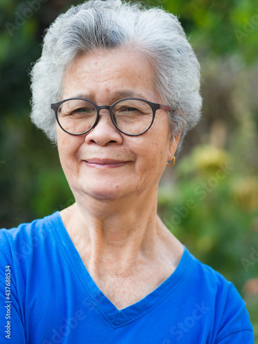 Portrait of an elderly Asian woman with short gray hair, smiling and looking at the camera while standing in a garden. Space for text. Aged people and healthcare concept