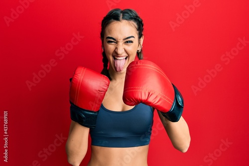 Young brunette girl using boxing gloves sticking tongue out happy with funny expression. © Krakenimages.com