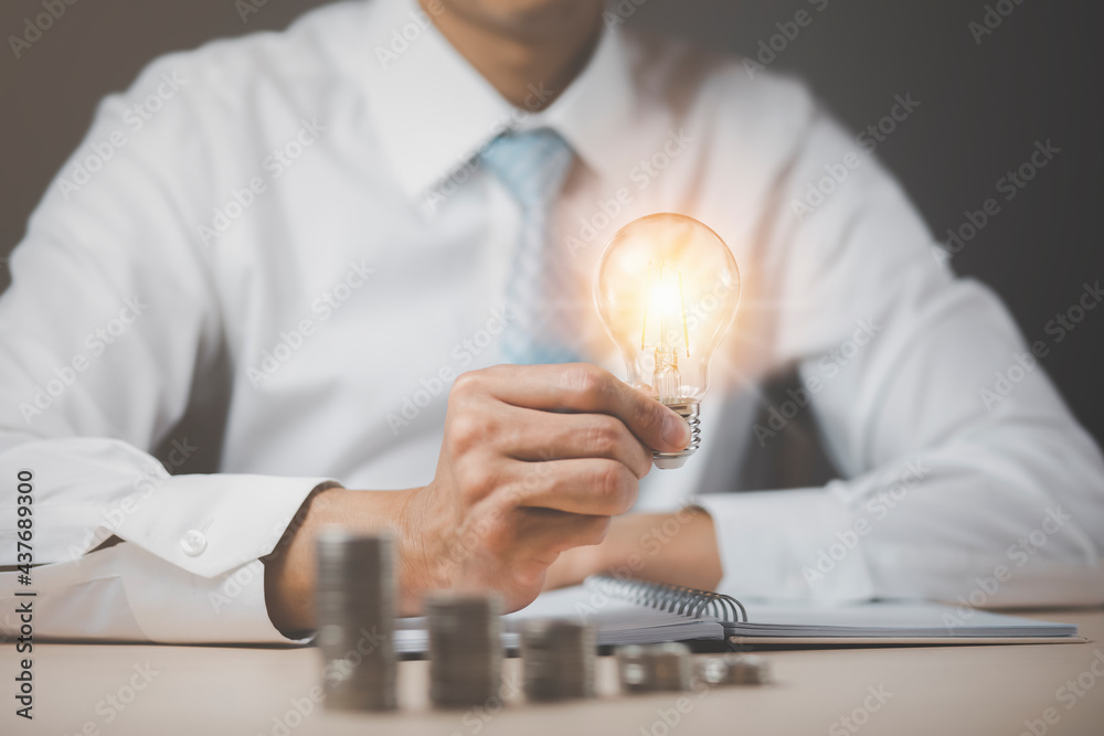 Businessman hand holding light bulb with line connect and Coins stack on the wooden table, Saving ideas and investment budget, Creative ideas concept of saving money  concept, Copy space