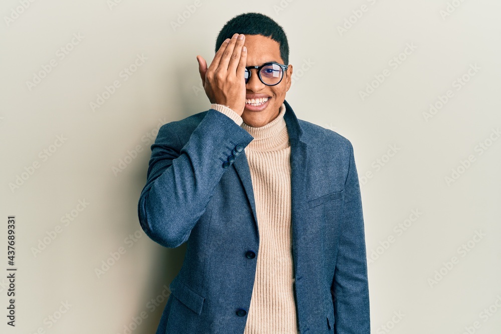 Young handsome hispanic man wearing elegant clothes and glasses covering one eye with hand, confident smile on face and surprise emotion. Young handsome hispanic man wearing elegant clothes and glasses covering one eye with hand, confident smile on face and surprise emotion.