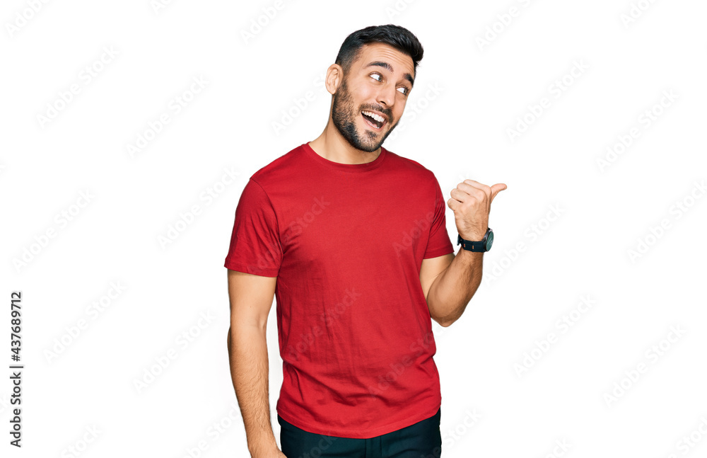 Young hispanic man wearing casual clothes smiling with happy face looking and pointing to the side with thumb up. Young hispanic man wearing casual clothes smiling with happy face looking and pointing to the side with thumb up.