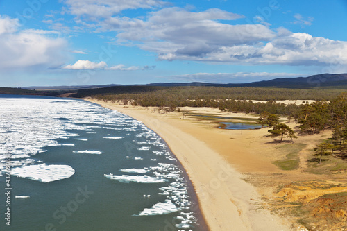 Baikal Lake in May. View of the sandy beach of the Sarayskiy Gulf with melting ice near the coast. Beautiful spring landscape. Natural background. Travels at springtime