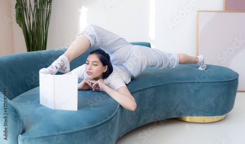 Flexible beautiful young woman reading a book on the sofa. Concept of individuality, creativity and education