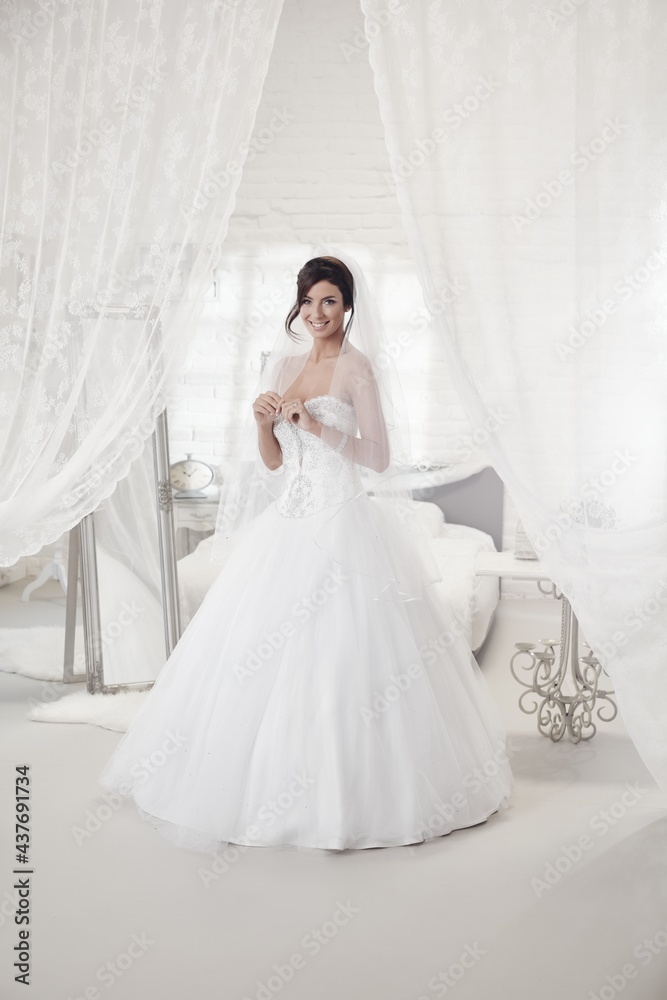 Beautiful bride standing in bedroom in wedding dress, smiling happy. Full size. Beautiful bride standing in bedroom in wedding dress, smiling happy. Full size.