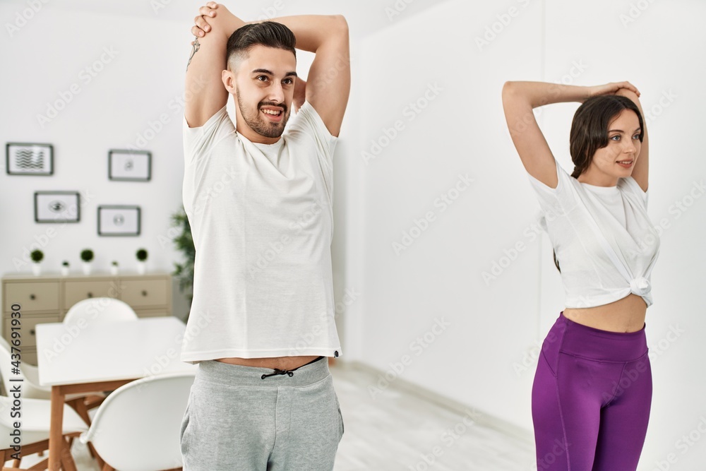 Fototapeta premium Young hispanic couple doing sport streching arms at home