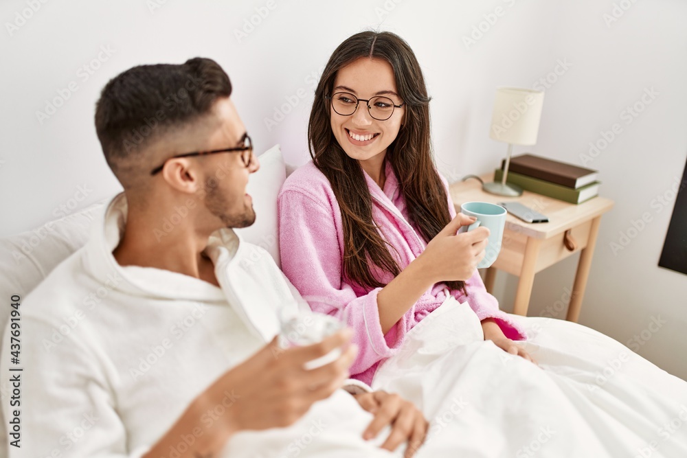 Young hispanic couple drinking coffee and water lying in bed at home. Young hispanic couple drinking coffee and water lying in bed at home.