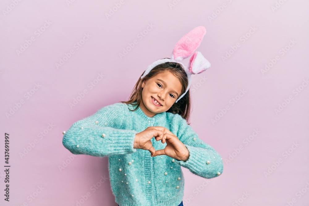 Little beautiful girl wearing cute easter bunny ears smiling in love doing heart symbol shape with hands. romantic concept. Little beautiful girl wearing cute easter bunny ears smiling in love doing heart symbol shape with hands. romantic concept.