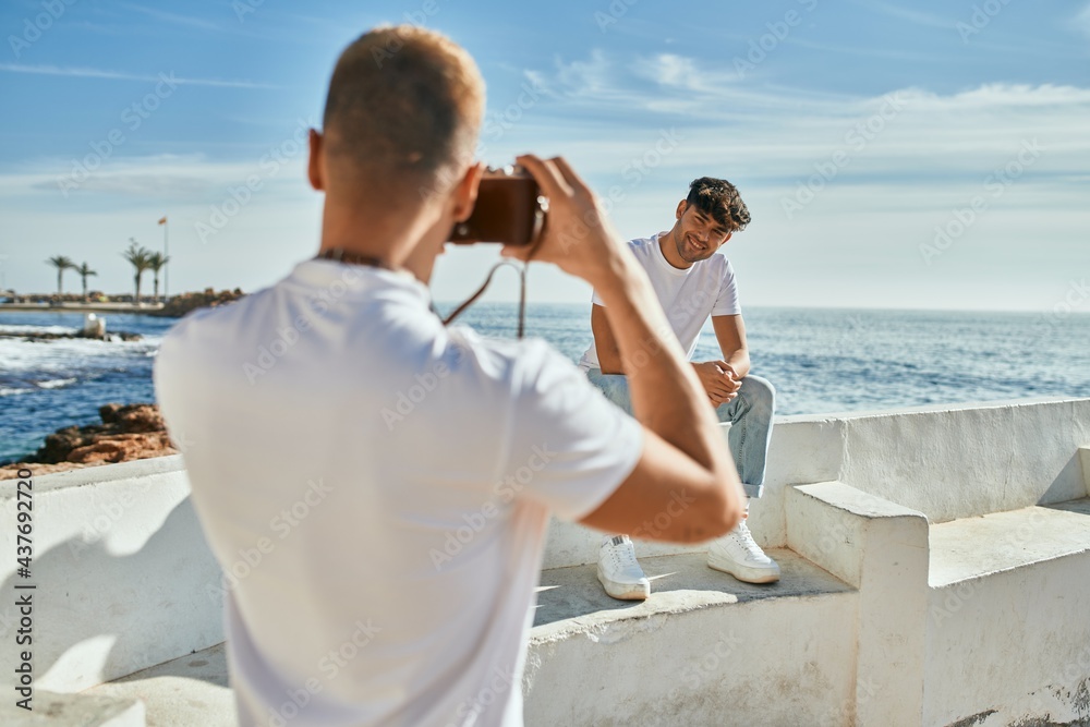 Man taking photos of his boyfriend in front of the sea.