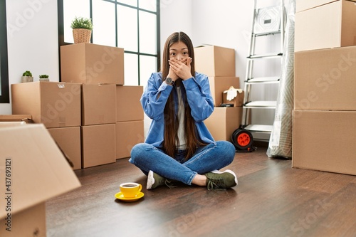 Fotografie Young chinese girl sitting on the floor at new home shocked covering mouth with hands for mistake