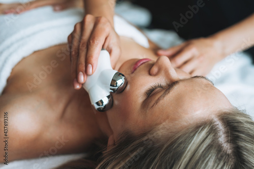 Fotografía Young blonde woman enjoys facial massage with microcurrent facial massager in spa, treat yourself