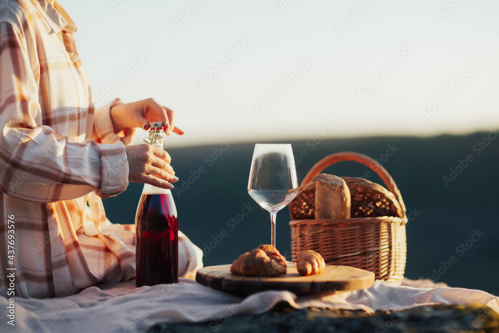 Woman opens the bottle of wine in the mountain at summer picnic.